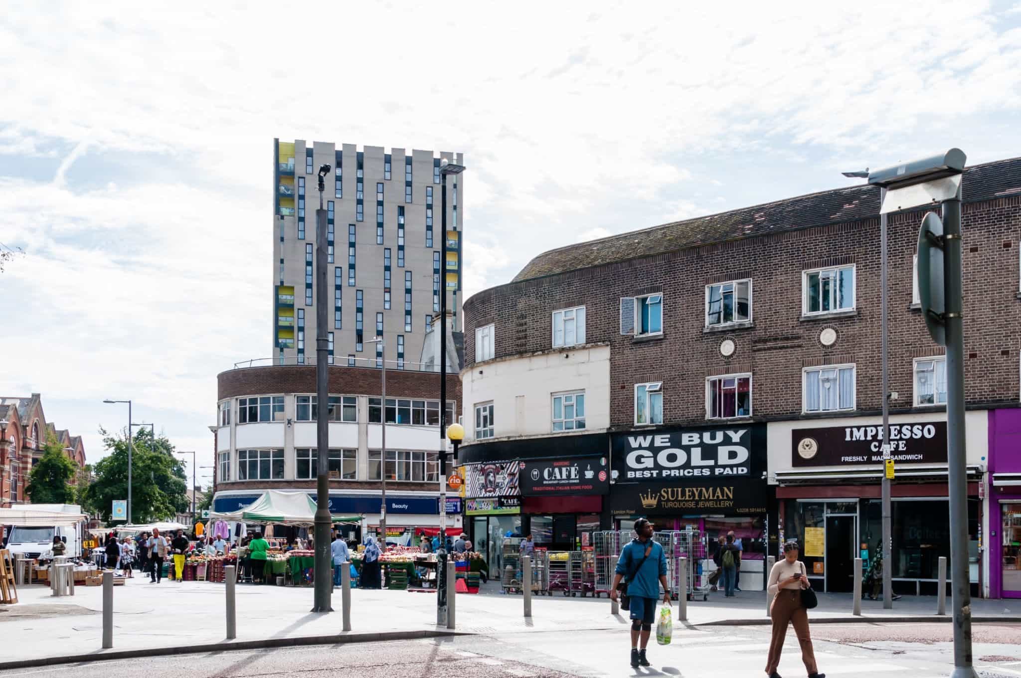 An authentic, documentary-style photograph capturing the utilitarian exterior of small business units and an industrial park near the River Thames in Dagenham, East London. A white, unbranded delivery van is parked near a loading bay under an overcast sky