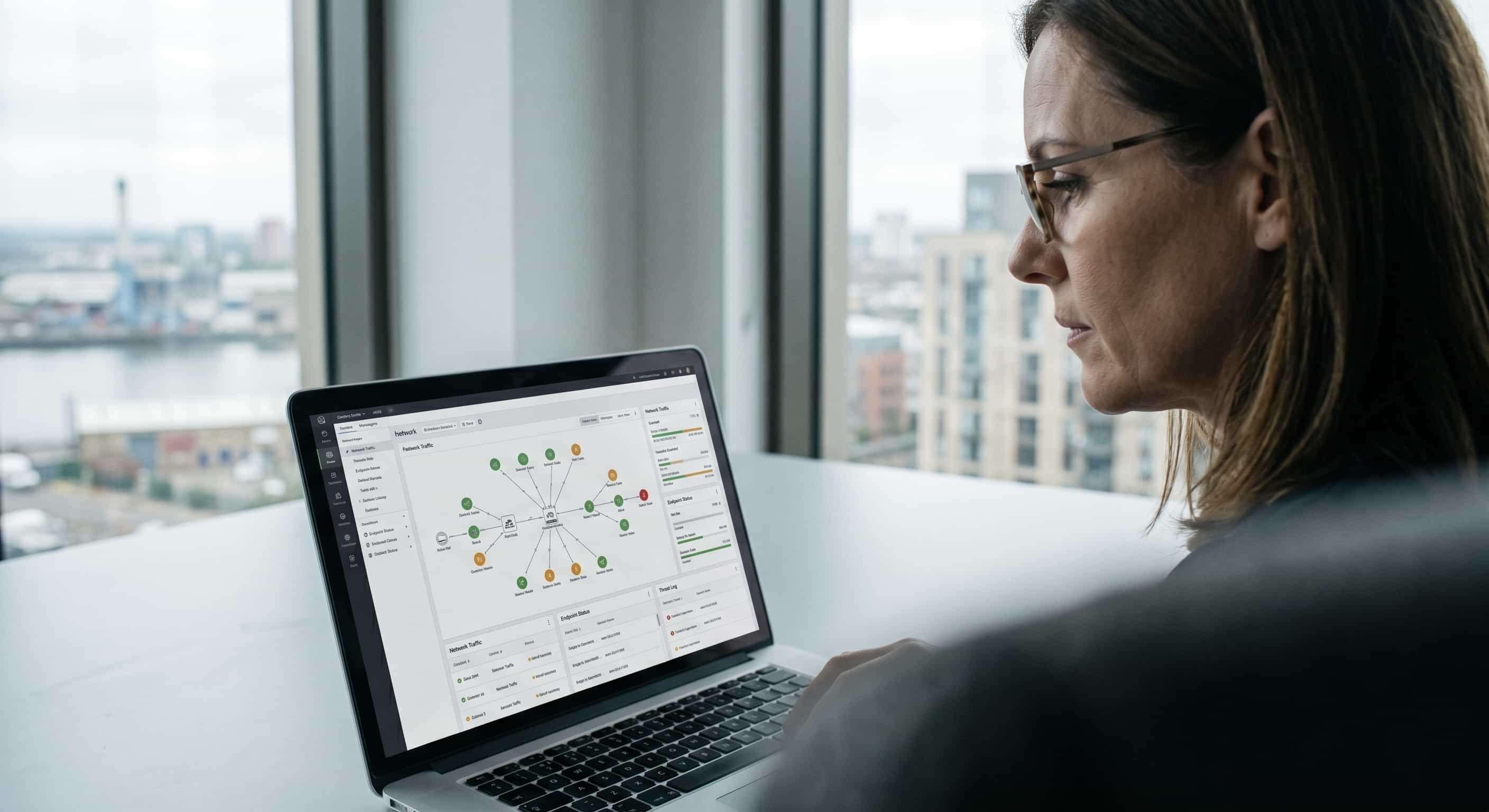 An SME director in Barking reviews a clean, realistic network traffic and endpoint cyber security monitoring dashboard on a laptop.